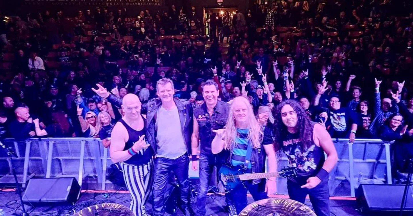 Maiden United posing on stage in front of a cheering crowd.