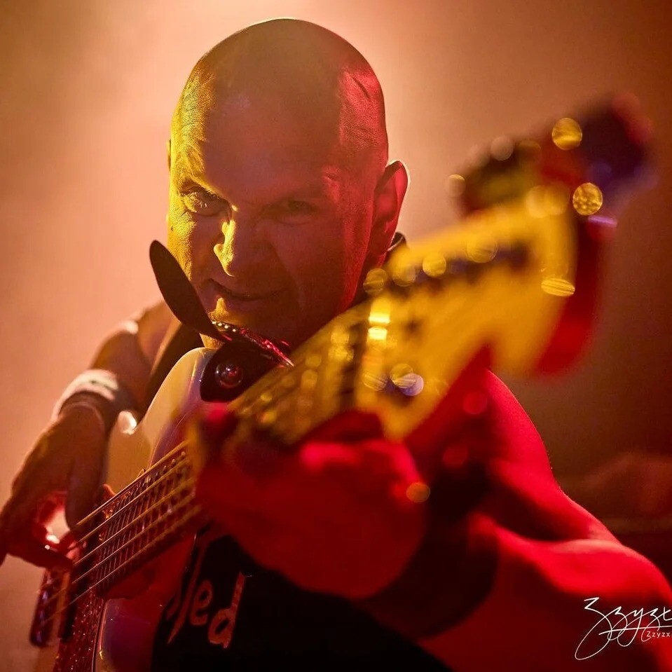 Danny Knapp intensely playing bass guitar on stage under dramatic lighting.