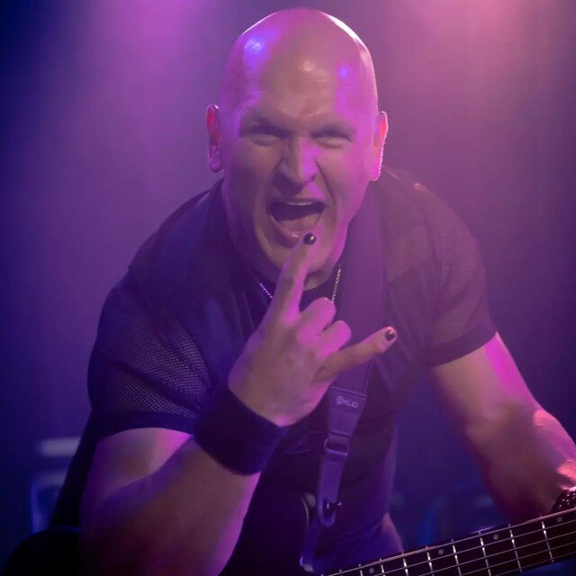 Danny Knapp flashing the rock hand sign under purple stage lights.